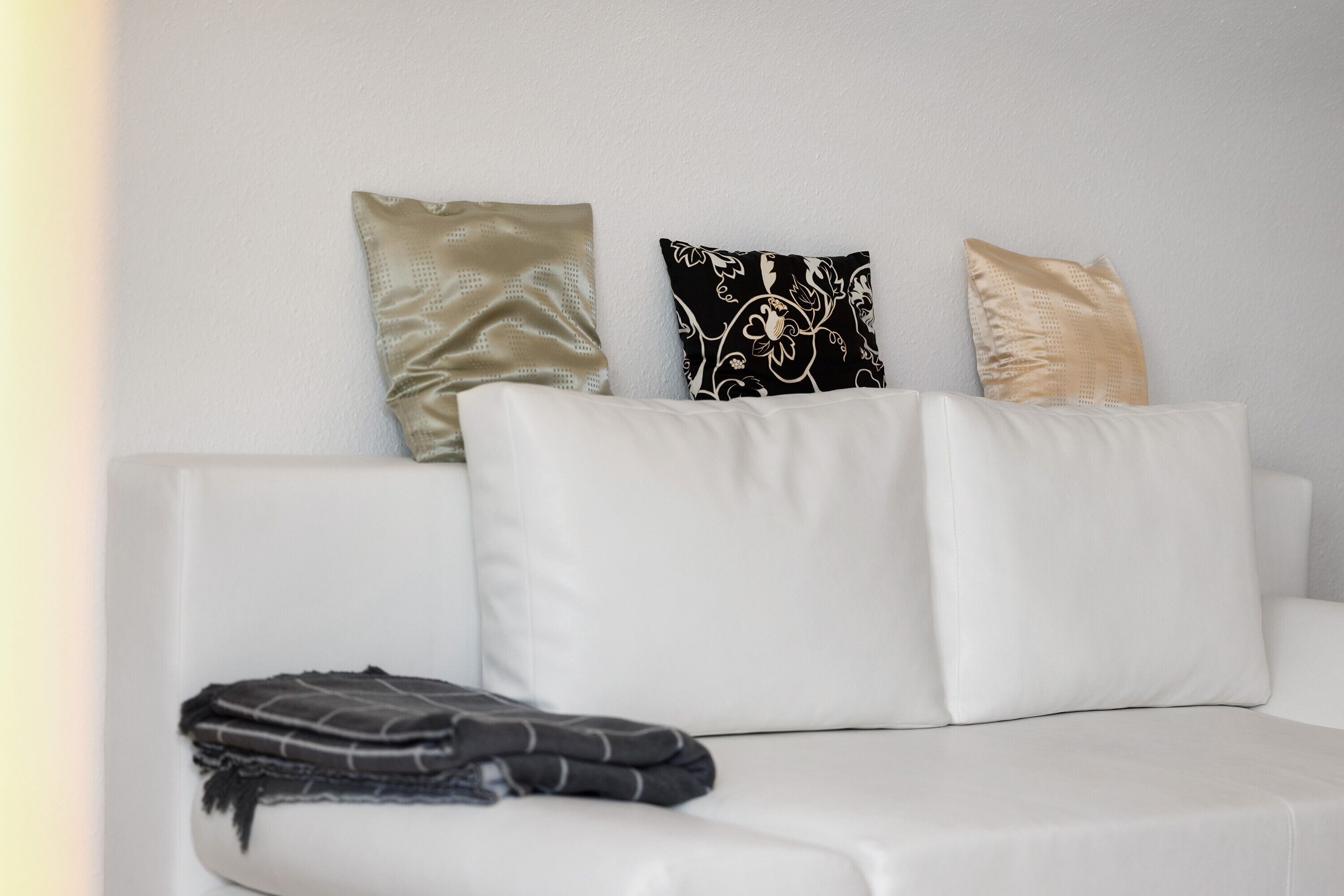 A white sofa with three pillows in different patterns and textures.