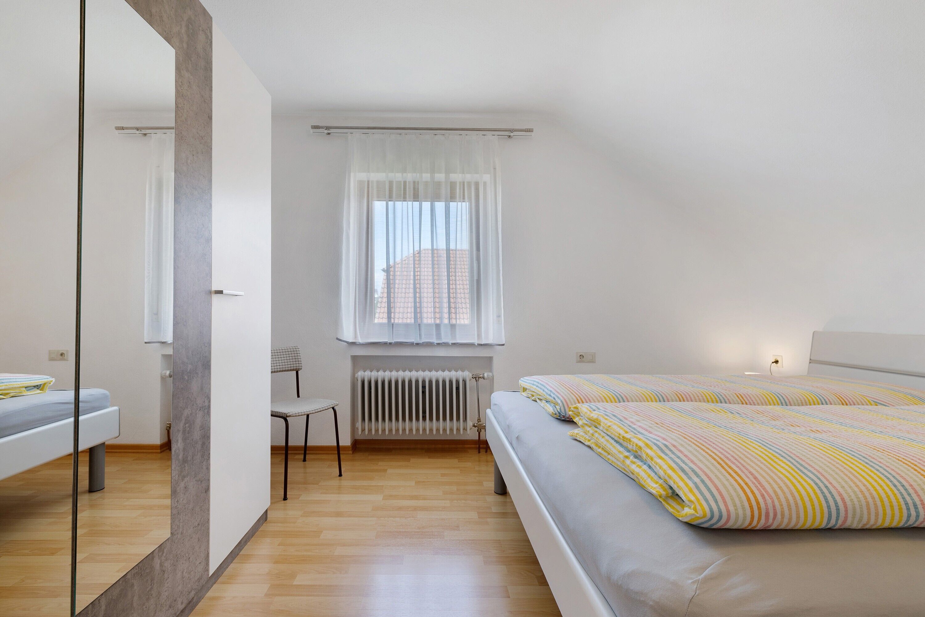 A bedroom with a bed, a chair, a radiator, and a window with curtains.