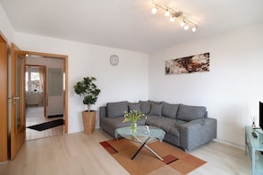 Un salon moderne avec un canapé gris, une table basse en verre, une plante en pot et un tableau accroché au mur.