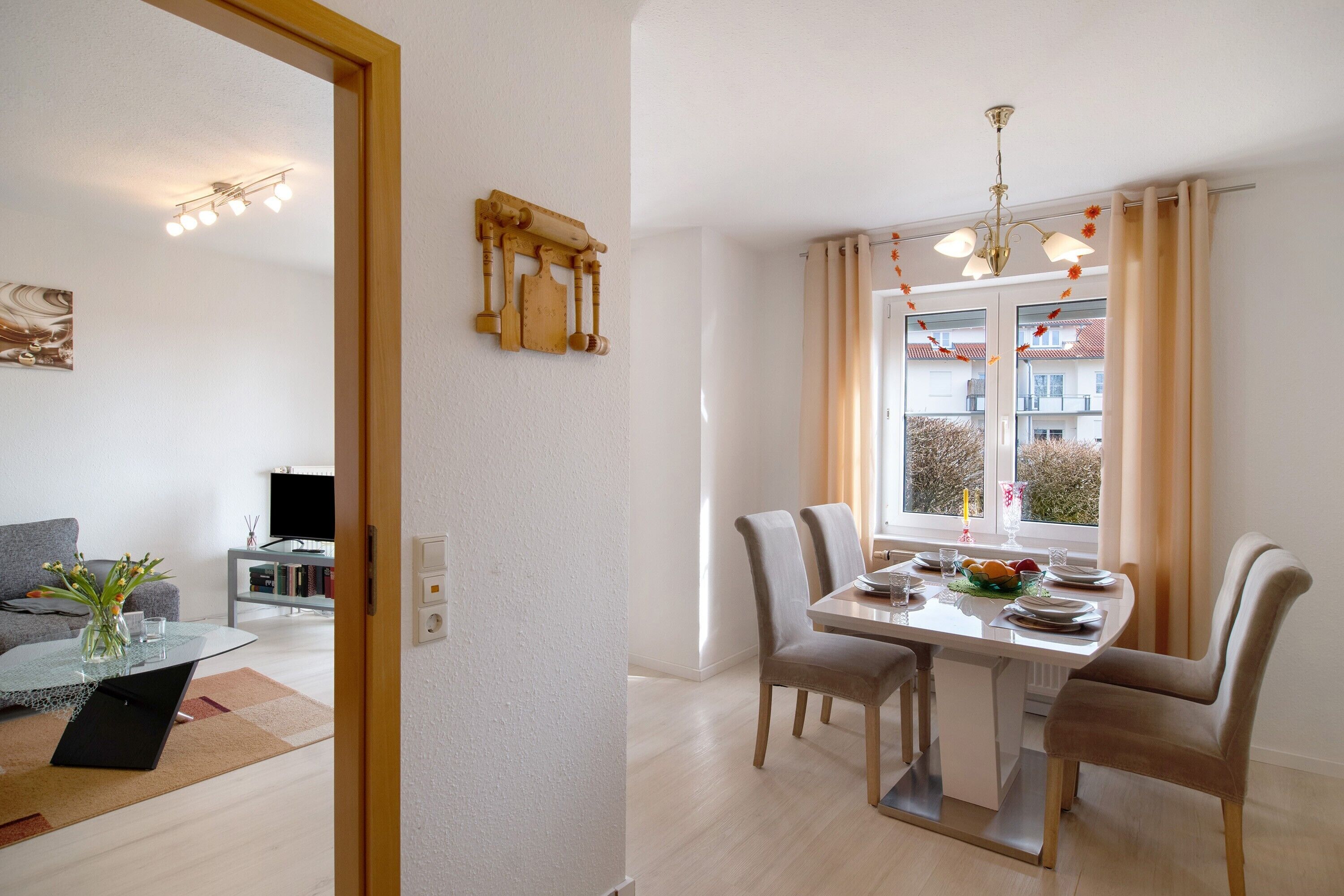 Ein Essbereich mit Tisch für vier Personen, einem Fenster mit Vorhängen und Blick auf Gebäude.