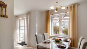 A dining area with a table set for two, a window with curtains, and a view of buildings outside. - Quiet Apartment in Bad Saulgau with Mountain View, Private Terrace and Wi-Fi (Bad Saulgau)
