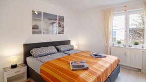 A bedroom with a bed, bedside table, nightstand, window with curtains, and wall-mounted artwork. - Quiet Apartment in Bad Saulgau with Mountain View, Private Terrace and Wi-Fi (Bad Saulgau)