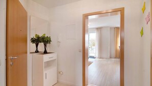 A room with a wooden door, a white cabinet with plants, a mirror, and a view of another room through a doorway. - Quiet Apartment in Bad Saulgau with Mountain View, Private Terrace and Wi-Fi (Bad Saulgau)