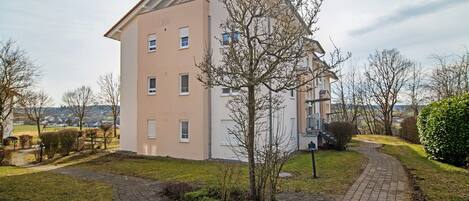 A two-story residential building with a paved driveway and a small tree in the front yard.