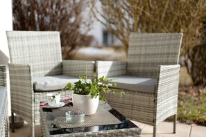 Un espace extérieur aménagé avec des meubles en osier, comprenant une table, des chaises et un pot de fleurs.