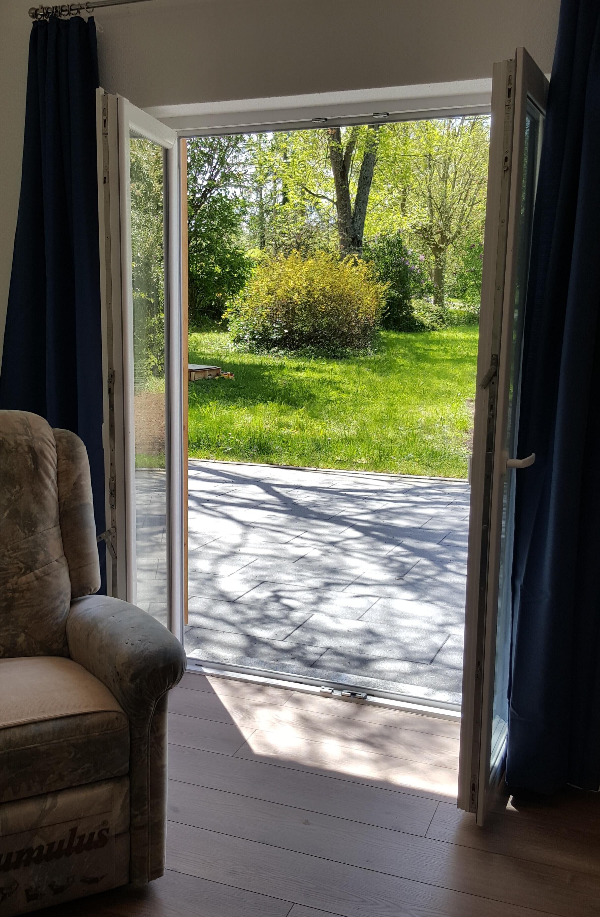 Une pièce dotée d’une porte-fenêtre coulissante donnant sur un espace extérieur aménagé, avec une pelouse et des arbres.