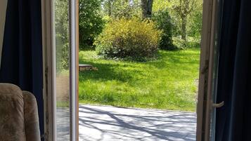 Une pièce dotée d’une porte-fenêtre coulissante donnant sur un espace extérieur aménagé, avec une pelouse et des arbres.