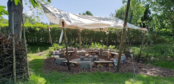 Un jardín con un pozo de fuego de piedra y una estructura cubierta.