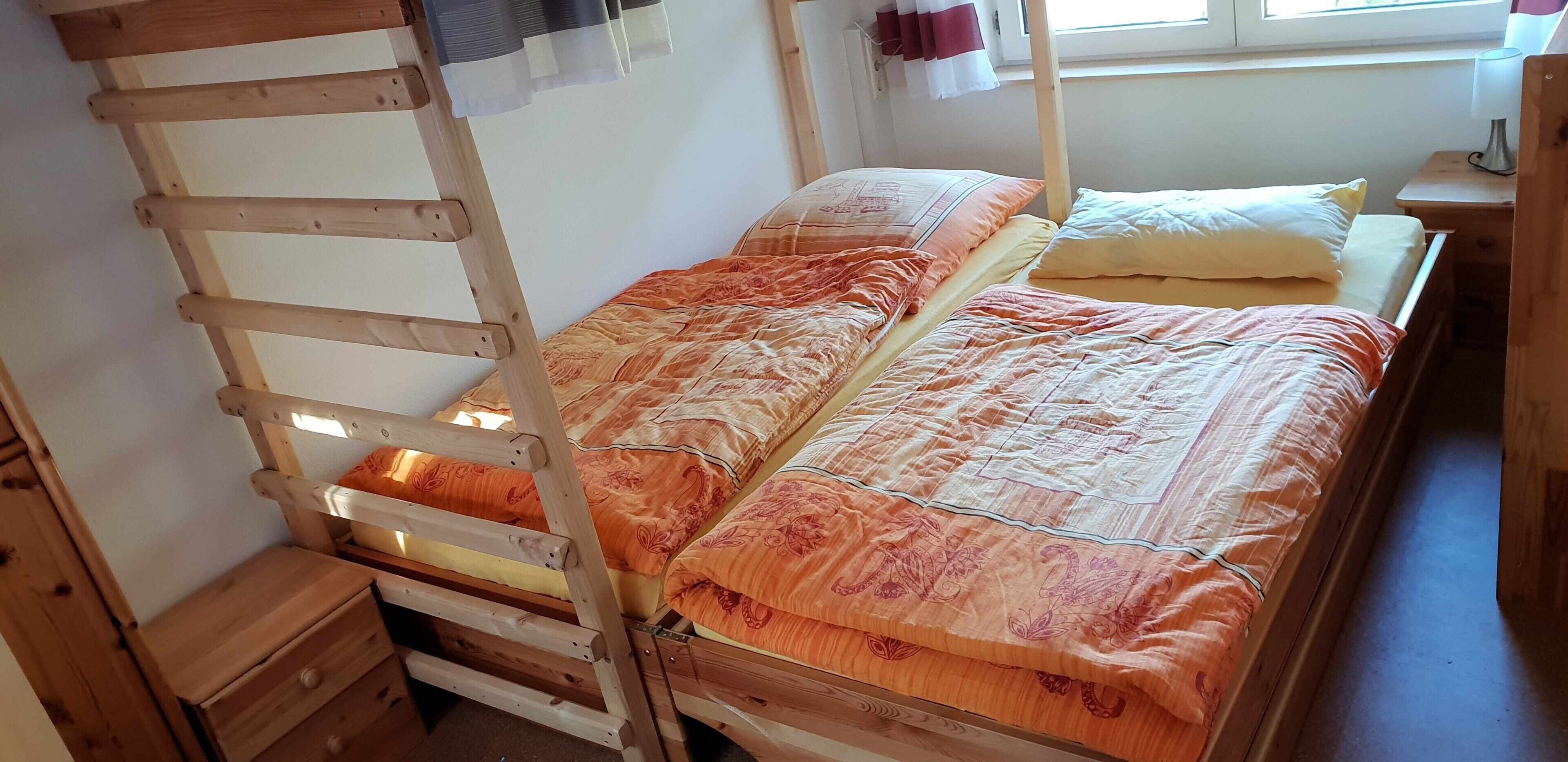 Ein Etagenbett mit einer Leiter, ein Nachttisch und ein Fenster mit Vorhängen.