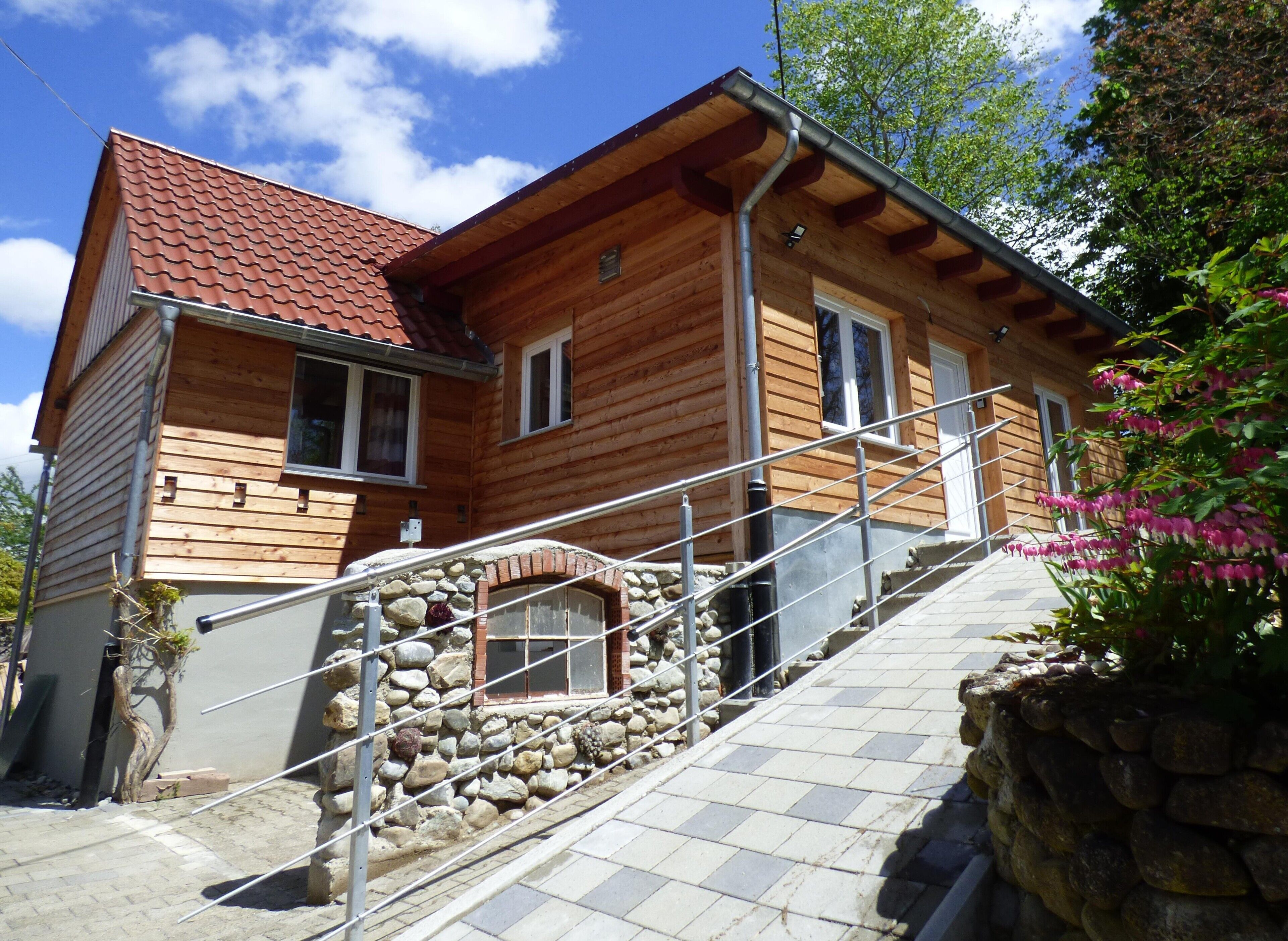 A wooden house with a red roof, stone steps, and a metal railing.