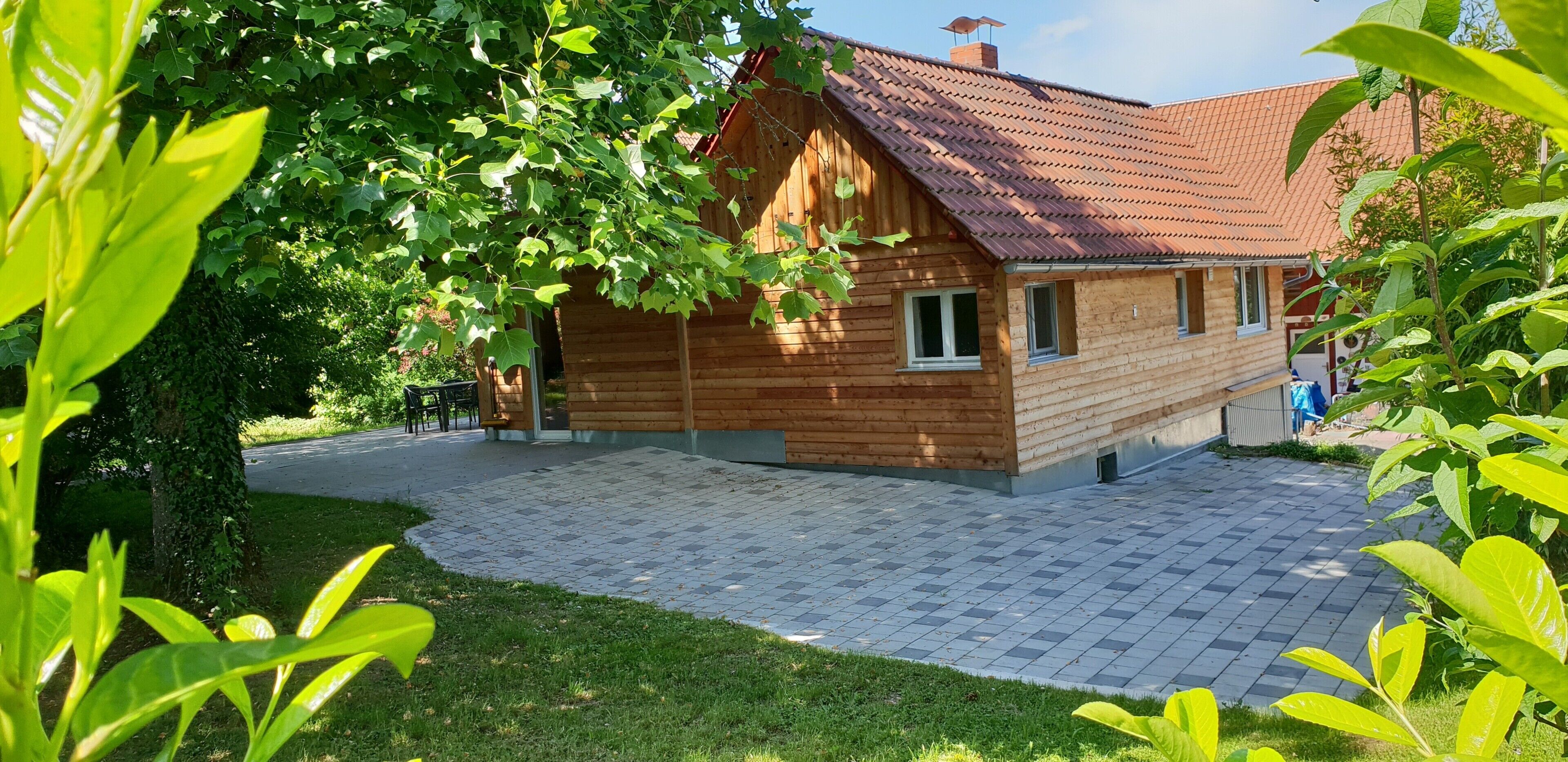 Una casa in legno con tetto rosso, vialetto lastricato e giardino con vegetazione verde.