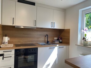 A modern kitchen with white cabinets, a wooden countertop, a black stove, and a window with plants.