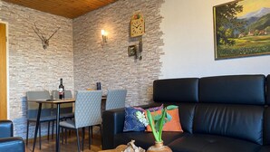 Una sala de estar con pared de piedra, un sofá de cuero negro, una mesa de comedor con sillas y un cuadro en la pared.