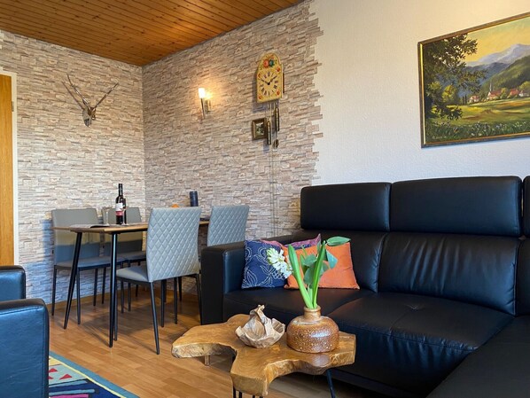 A living room with a stone wall, a black leather sofa, a dining table with chairs, and a painting on the wall.