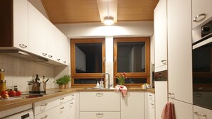 A modern kitchen with white cabinets, a wooden countertop, a built-in oven, and a washing machine.
