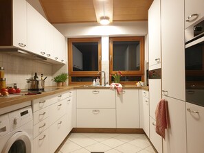 A modern kitchen with white cabinets, a wooden countertop, a built-in oven, and a washing machine.