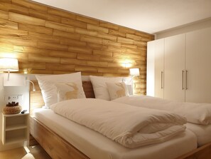 A bedroom with a wooden headboard, two bedside tables with lamps, a bed with white bedding, and a wardrobe.