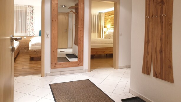 A hotel room with a wooden wardrobe, a mirror, a bed, and a bathroom visible through an open door.