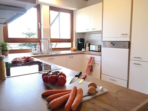 A modern kitchen with white cabinets, a built-in microwave, and a window with a view of trees.