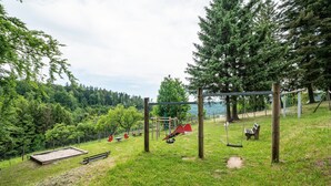 A playground with swings, a slide, and a sandbox in a park with trees and a hill. - Naturerlebnishaus Gaistal 32 with Nature Views (Bad Herrenalb)