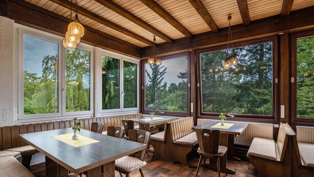 A dining area with wooden tables and benches, large windows with a view of trees, and hanging pendant lights. - Naturerlebnishaus Gaistal 32 with Nature Views (Bad Herrenalb)