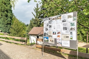 Un panneau d’affichage présentant des photos et des textes d’époque, une clôture en bois et un petit bâtiment avec un toit rouge.