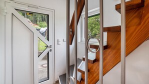 A modern interior with a wooden staircase, a glass door leading outside, and a view of greenery. - Naturerlebnishaus Gaistal 32 with Nature Views (Bad Herrenalb)