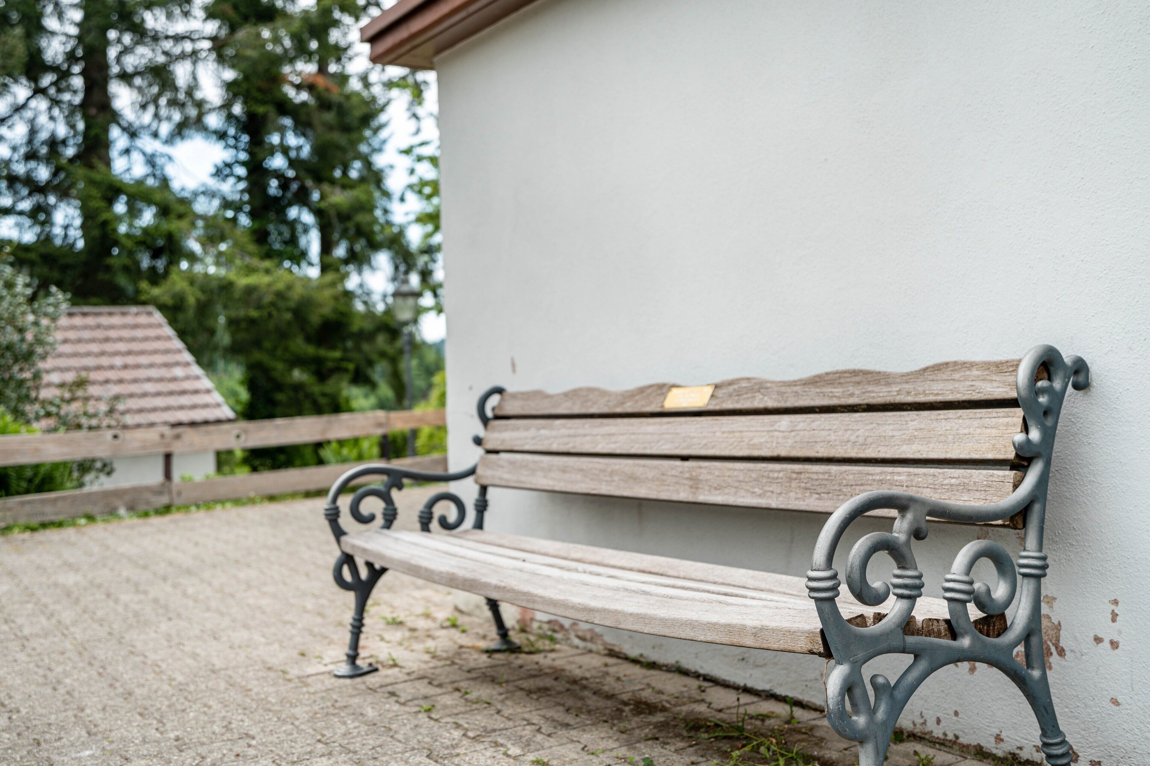 A wooden bench with metal armrests against a white wall.