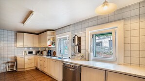A modern kitchen with white cabinets, a stainless steel dishwasher, and a window with a view of a garden. - Naturerlebnishaus Gaistal 32 with Nature Views (Bad Herrenalb)