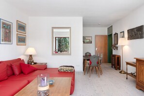 A living room with a red sofa, a wooden coffee table, a dining area with a table and chairs, and a mirror on the wall.