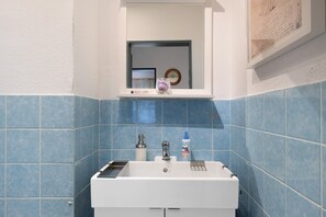 A bathroom with a white sink, blue tiles, a mirror, and a framed picture on the wall.