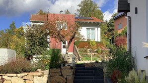 Ein gepflasterter Weg führt zu einem Haus mit einer Steinmauer und einer Rasenfläche.