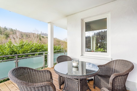 A covered outdoor seating area with wicker chairs, a glass table, and a view of greenery and hills.