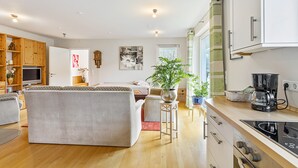 Ein modernes Wohnzimmer mit einer Couch, einem Fernseher, Holzschränken und einer Küchenzeile mit einer Kaffeemaschine.