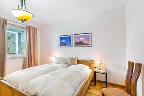 Quarto com cama de madeira, duas mesas de cabeceira com luminárias, uma janela com cortinas e duas fotos emolduradas na parede.