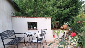 Eine Terrasse mit Tisch und Stühlen, ein kleines Fenster und ein Garten mit Pflanzen und einer Rose.