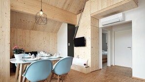 Interior de madera con comedor, sillas, una mesa preparada para dos personas y un televisor montado en la pared.