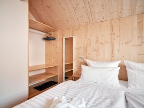 Un dormitorio con techo de madera, una cama con ropa de cama blanca, un armario de madera y una mesita de noche.