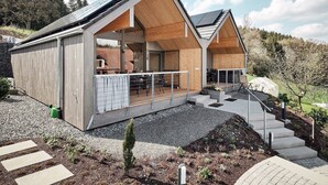 Una casa moderna con fachada de madera, ventanas amplias y un espacio exterior cubierto.