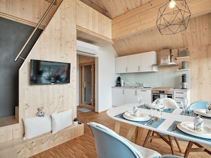 Una cocina moderna con gabinetes blancos, un comedor con mesa redonda y una zona de estar acogedora con sofá y televisor.