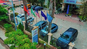 L’entrée d’un hôtel, avec un panneau indicateur, un espace de stationnement délimité par une clôture et plusieurs drapeaux.