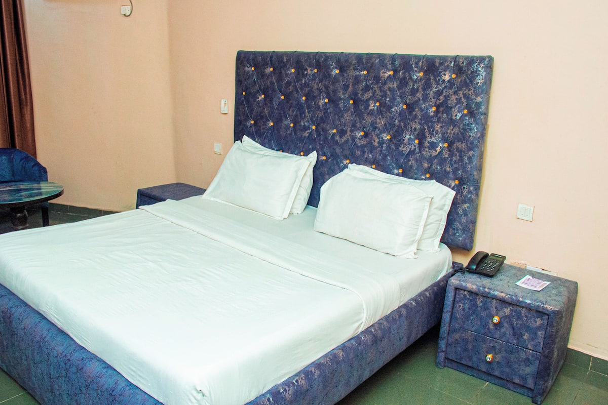 Une chambre d’hôtel avec un grand lit, une table de chevet avec un téléphone et un petit tiroir.