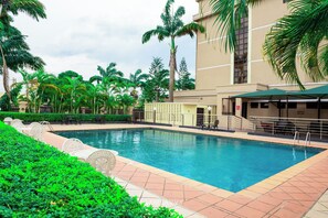 A swimming pool surrounded by palm trees and a building with a beige facade. - DEES HOTELS APARTMENT & SUITES (Lagos)