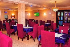 A restaurant with red chairs and blue tablecloths, a TV mounted on the wall, and a chandelier. - DEES HOTELS APARTMENT & SUITES (Lagos)