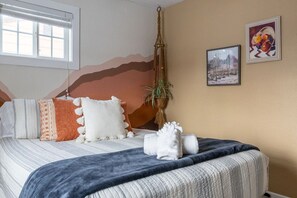 A bedroom with a bed, pillows, a hanging plant, and artwork on the wall.