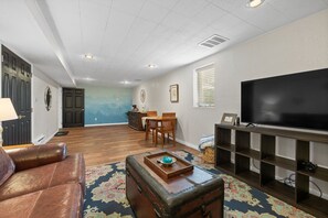 Una sala de estar con televisor, sofá de cuero, mesa de centro de madera y alfombra estampada.