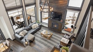 A spacious living area with a fireplace, large windows, and a cozy seating arrangement. - Modern Mountain Retreat (Sturgis)