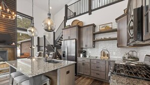 A modern kitchen with granite countertops, stainless steel appliances, and a central island with bar stools. - Modern Mountain Retreat (Sturgis)