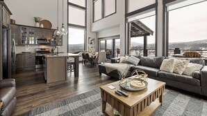 A spacious living area with a large window, a kitchen with modern appliances, and a cozy seating area with a leather couch and a coffee table. - Modern Mountain Retreat (Sturgis)
