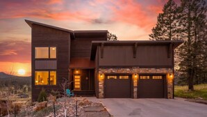A modern two-story house with a garage, a stone foundation, and a view of the sunset. - Modern Mountain Retreat (Sturgis)